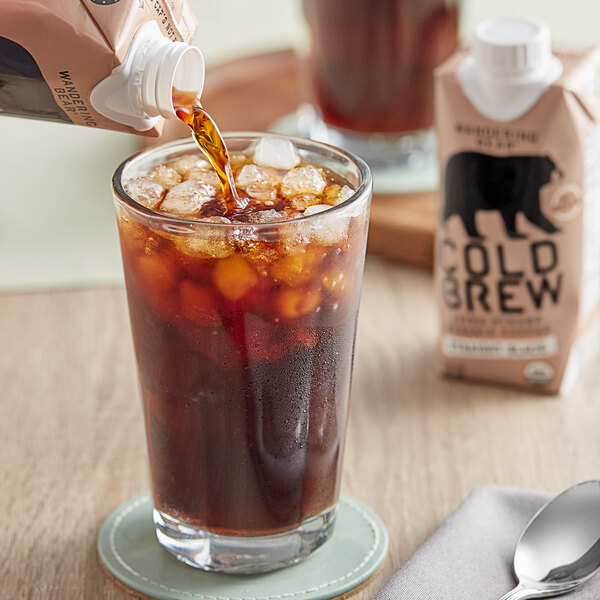 A person pouring Wandering Bear Organic Straight Black Cold Brew Coffee into a glass with ice.