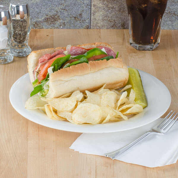 A sandwich with vegetables and meat on a Thunder Group ivory melamine plate with potato chips.