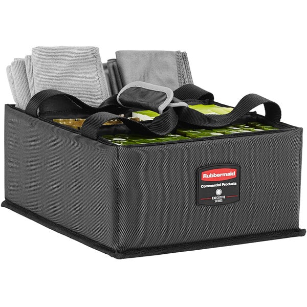 A Rubbermaid gray and black housekeeping caddy on a table with towels and other items inside.