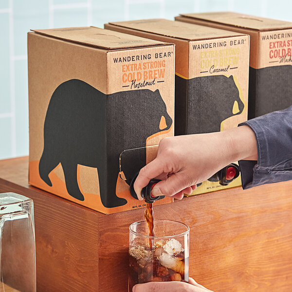 A hand pouring Wandering Bear Bag in Box Organic Hazelnut Cold Brew Coffee into a glass.