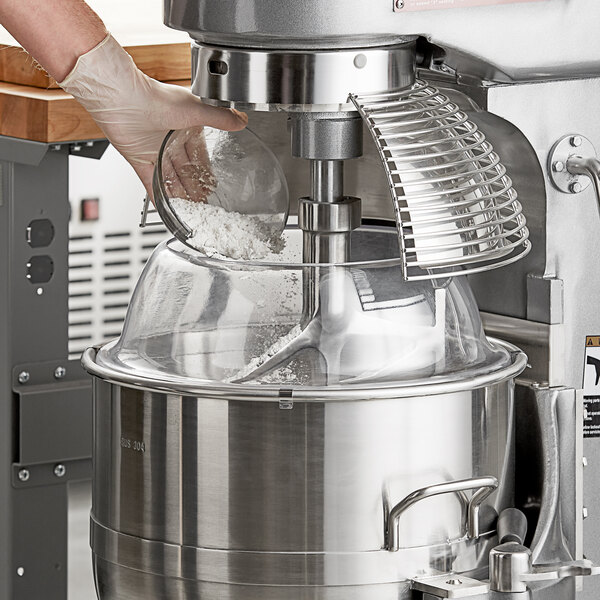 A person uses an Avantco mixer with a splash cover to mix flour in a bowl.