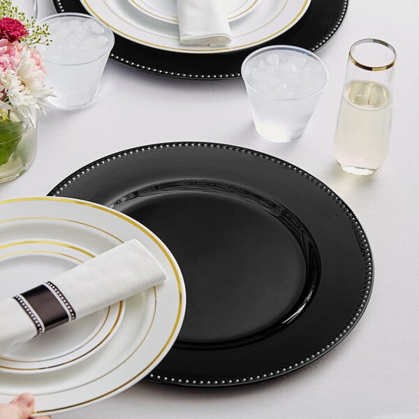 A white table set with a black beaded rim charger plate and white napkin.