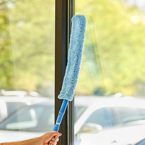 A hand holding a Lavex 24" Flex Wand Duster with a blue microfiber sleeve.