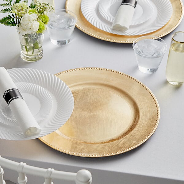 A table set with gold Choice charger plates, glasses, and white napkins.