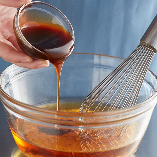 A hand pouring Lee Kum Kee Panda Brand Oyster Flavored Sauce into a glass bowl of liquid.