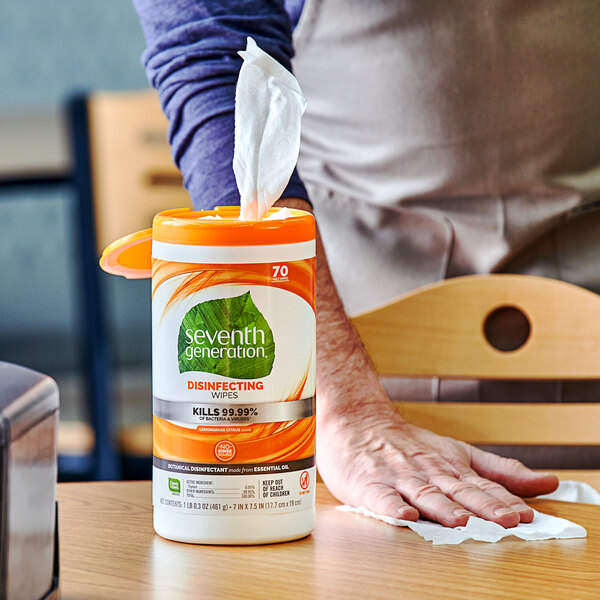 A person using Seventh Generation Lemongrass Citrus Disinfecting Wipes to clean a table.