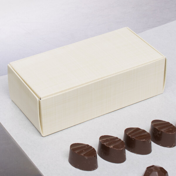 A group of chocolate covered chocolates in a white 1/2 lb. candy box with a lid.