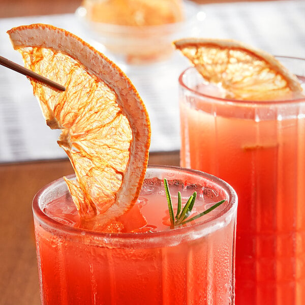 A close-up of two glasses of orange juice with dried grapefruit slices on top.