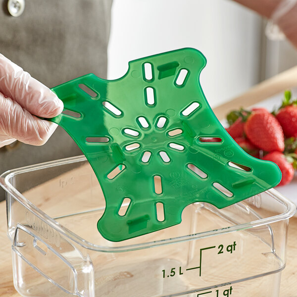 A person holding a green plastic tray with holes over a green Cambro container of strawberries.