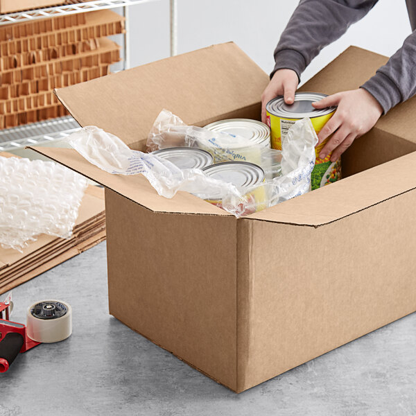 A person putting cans of food in a Lavex heavy-duty cardboard shipping box.