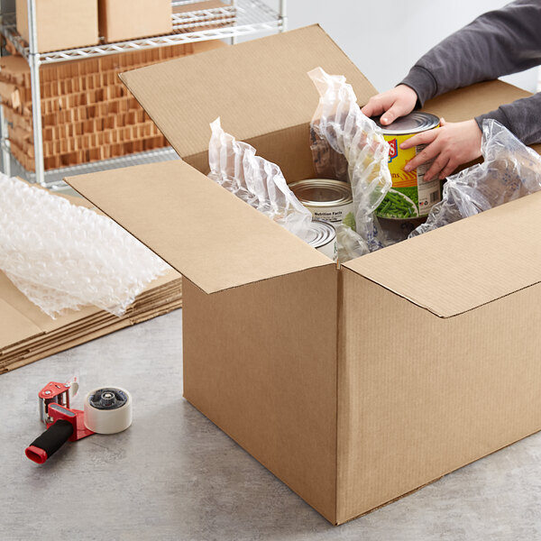 A hand packing a yellow container of food in a Lavex corrugated shipping box.