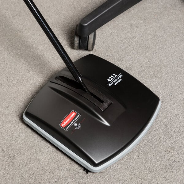 A Rubbermaid Executive Series floor sweeper with a black handle sitting on the floor.