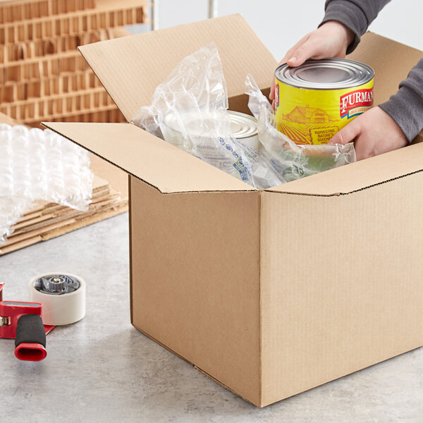 A person packing items in a Lavex heavy-duty corrugated shipping box with a can of food.