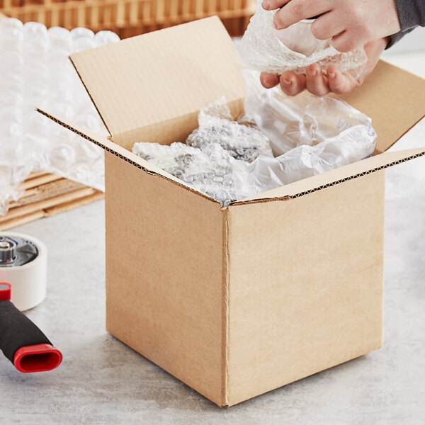 A hand putting a plastic bottle into a Lavex heavy-duty cardboard shipping box.