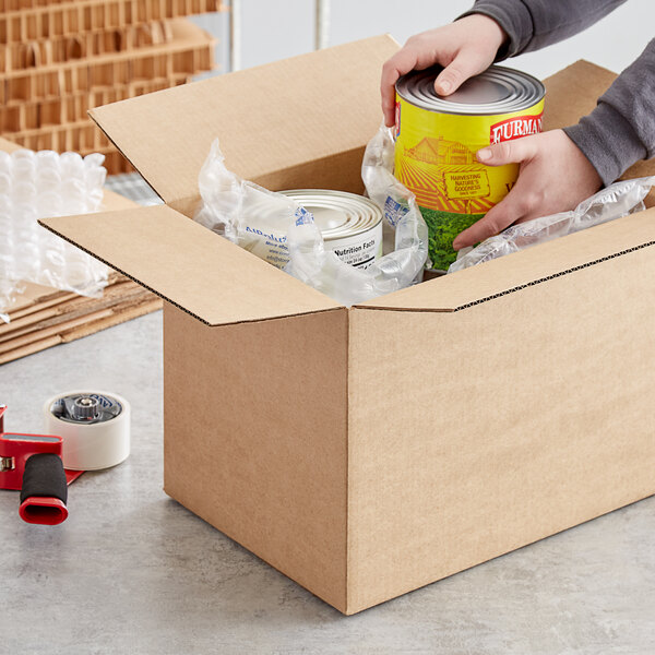 A person holding a Lavex heavy-duty corrugated cardboard box with cans of food inside.