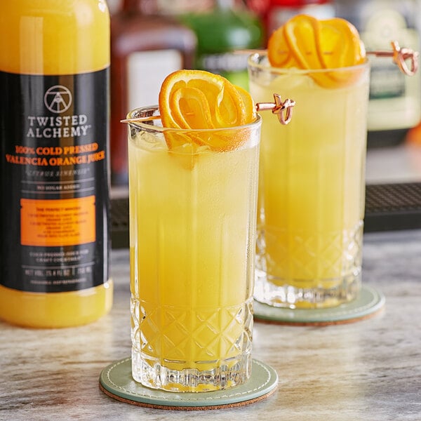Two glasses of Twisted Alchemy Valencia Orange Juice with orange slices on top.