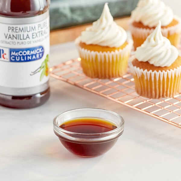 A cupcake with white frosting and a bowl of McCormick Culinary Pure Vanilla Extract.
