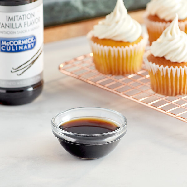 A cupcake with white frosting and a McCormick Culinary Imitation Vanilla bottle on a counter.