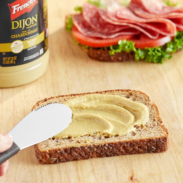A person spreading French's Dijon Mustard on a piece of bread.