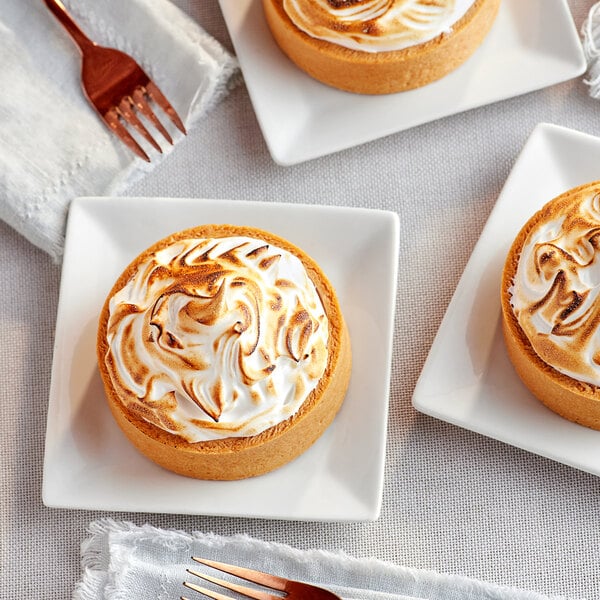 Three small pies with meringue on top of them on white plates.