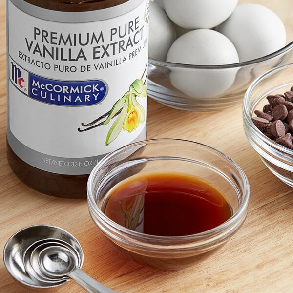 A bottle of McCormick Culinary Pure Vanilla Extract on a white counter next to a bowl of brown liquid and eggs.