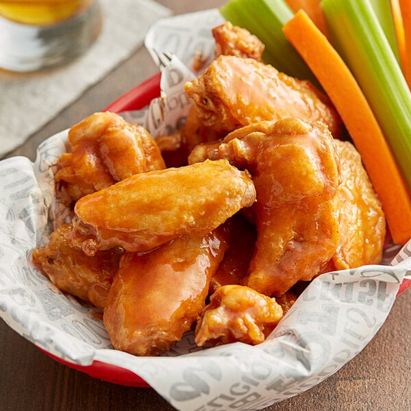 A red bowl of Frank's RedHot Original sauce with chicken wings, celery, and carrots.