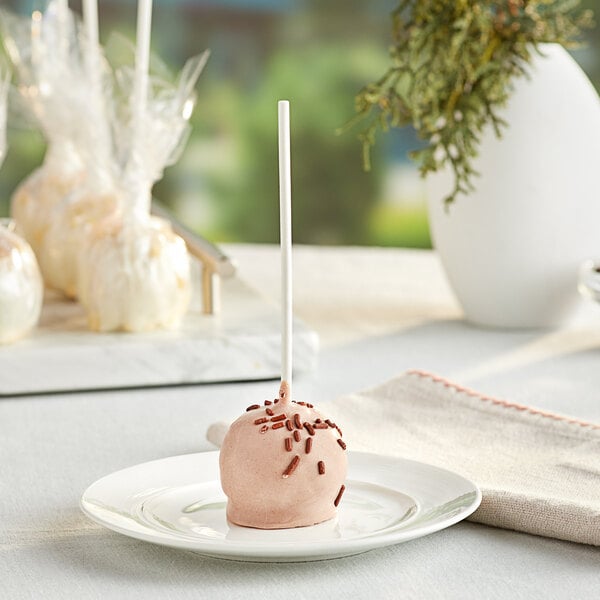 A chocolate covered cake pop with brown sprinkles on a white plate.
