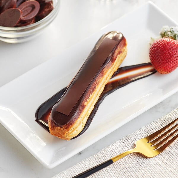 A white plate with a chocolate covered eclair and strawberries drizzled with Valrhona Manjari dark chocolate.