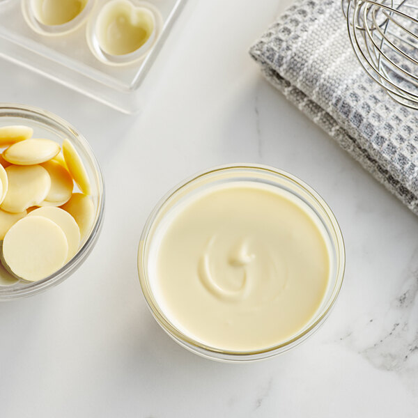 A bowl of white liquid chocolate next to a bowl of butter.