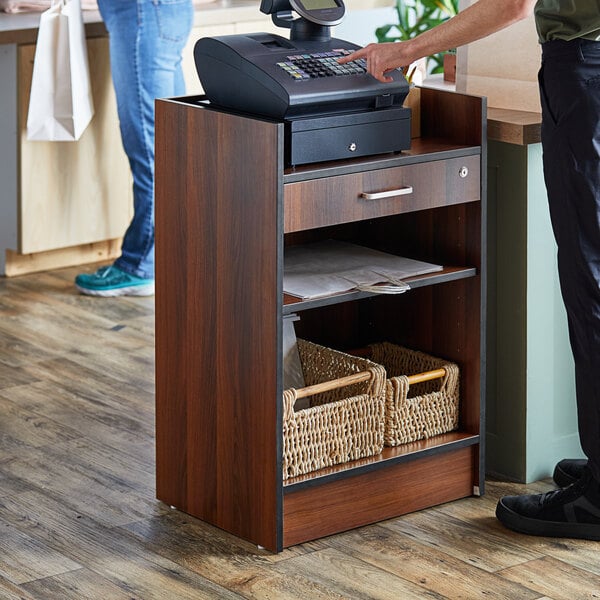 A person using a Lancaster Table & Seating walnut cash register stand.