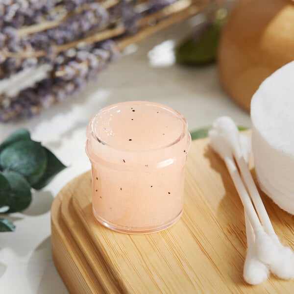 A clear jar of pink scrub on a wooden surface.