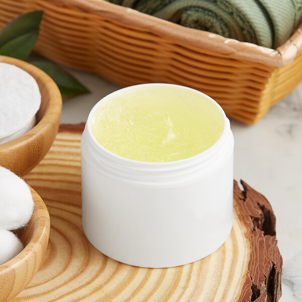 A white customizable jar filled with yellow liquid next to a basket of cotton.