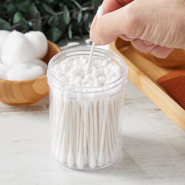 A hand holding a cotton swab in a clear polystyrene jar.