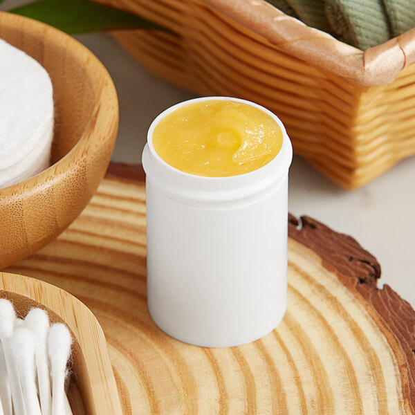 A white container with yellow substance in it next to a bowl of cotton buds and a basket of cotton.