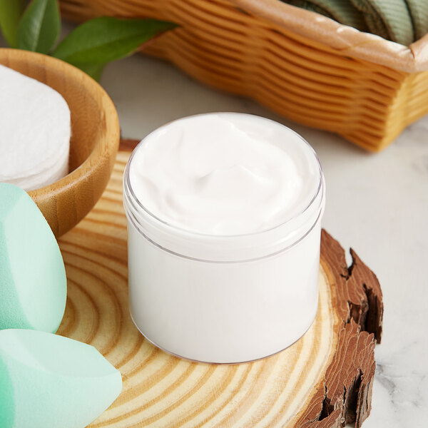A 4 oz. clear wide mouth jar of face cream next to sponges and a basket.