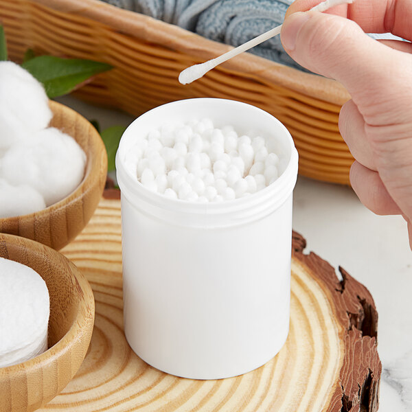 A person putting a cotton swab into a white jar.