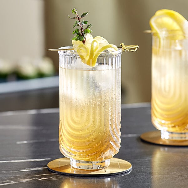 Two Acopa Zelda highball glasses with liquid and lemon slices on a table.