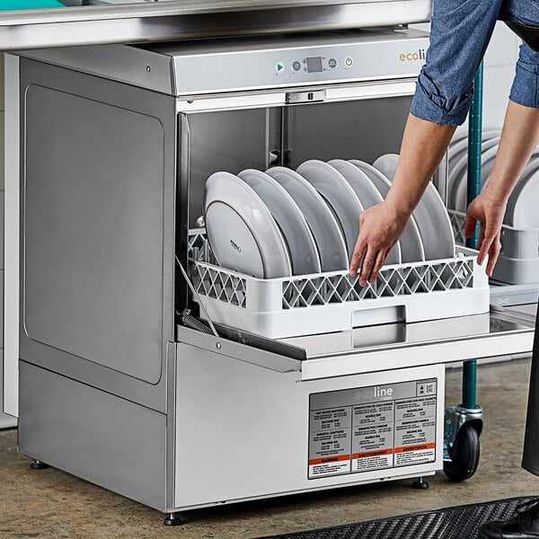A person putting plates in a Ecoline by Hobart undercounter dishwasher on a counter in a professional kitchen.