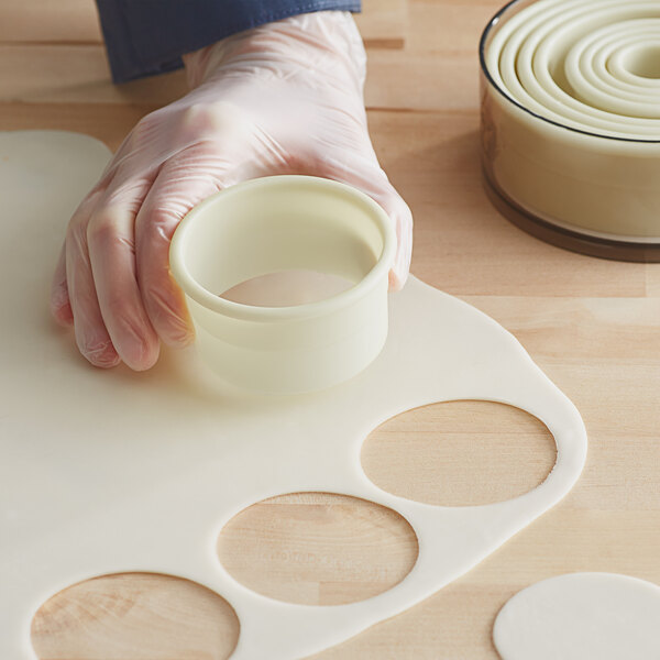 A person in gloves using a white Mercer Culinary round cutter to cut circles in dough.