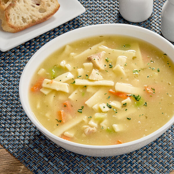 A bowl of Chef Francisco chicken noodle soup with bread on the side.