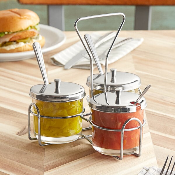 A metal wire condiment caddy with three glass jars with metal lids.