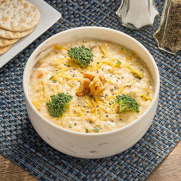 A bowl of TrueSoups broccoli cheddar soup with crackers and cheese on a table.