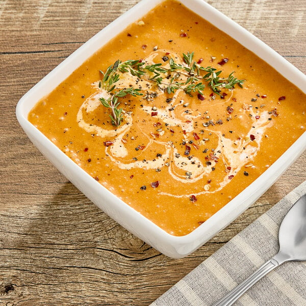 A bowl of Chef Francisco Roasted Red Pepper and Gouda soup with herbs on top.