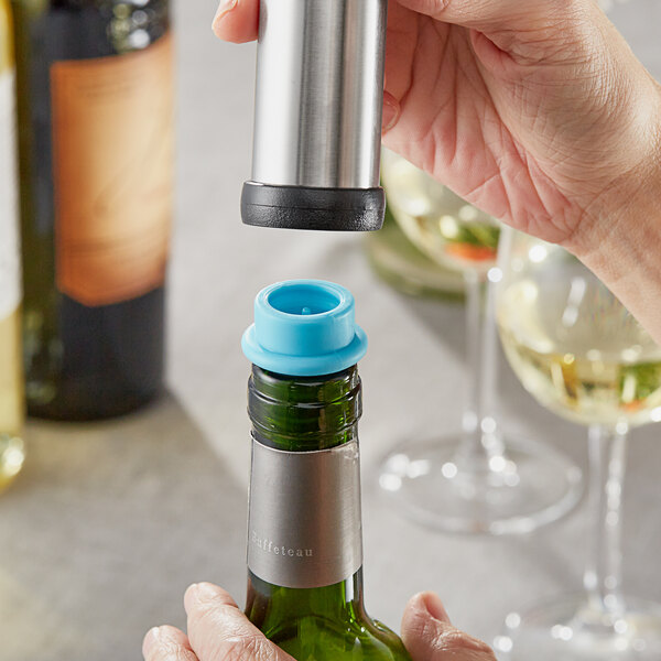 A hand using an Acopa blue vacuum wine stopper to seal a bottle of wine.