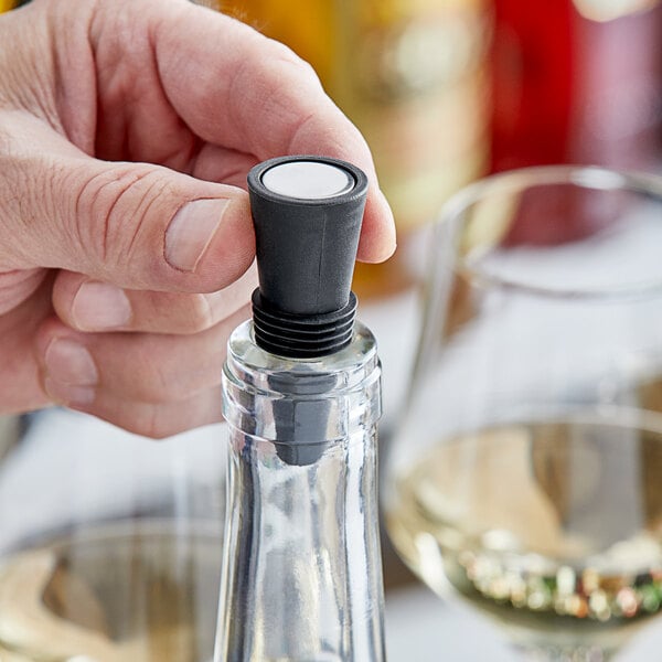 A hand holding a bottle of wine with an Acopa black wine stopper in it.