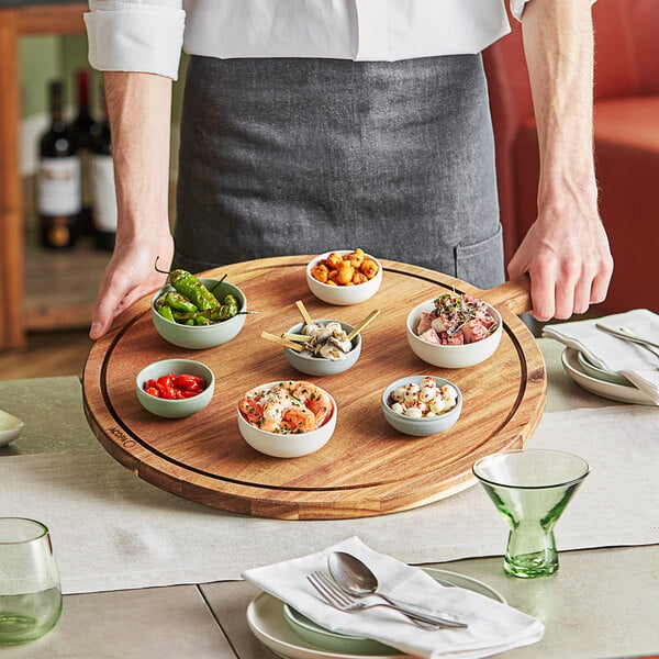 A chef holding an Acopa acacia wood serving board with bowls of shrimp and red food.