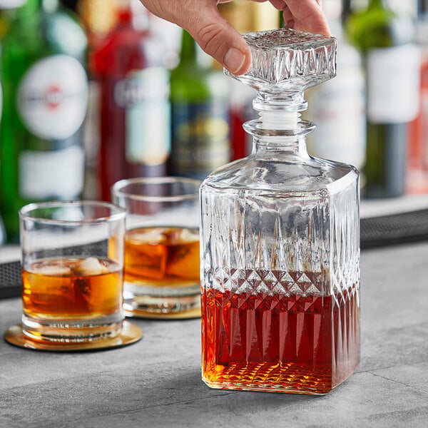 A hand pouring amber whiskey into an Acopa Cut Glass Whiskey Decanter.