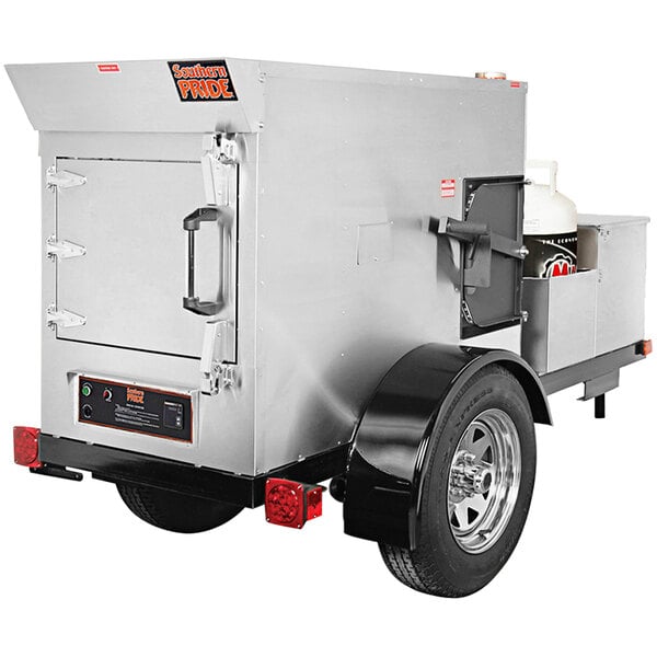 A silver Southern Pride stainless steel rotisserie smoker on a small trailer.