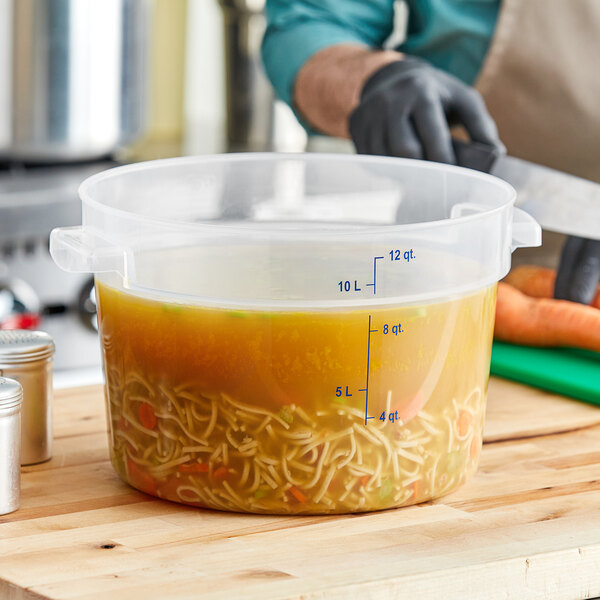 A person in a professional kitchen using a Carlisle translucent plastic container to store noodles.