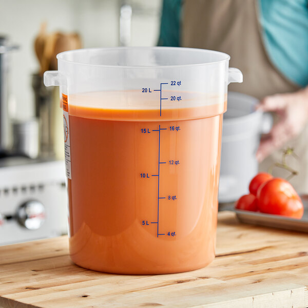 A woman holding a Carlisle translucent round food storage container with orange liquid in it.